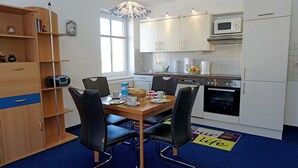 Eine moderne Küche mit weißen Schränken, einer Mikrowelle und einem Backofen. Ein Esstisch mit Stühlen und ein blauer Teppich sind ebenfalls vorhanden.