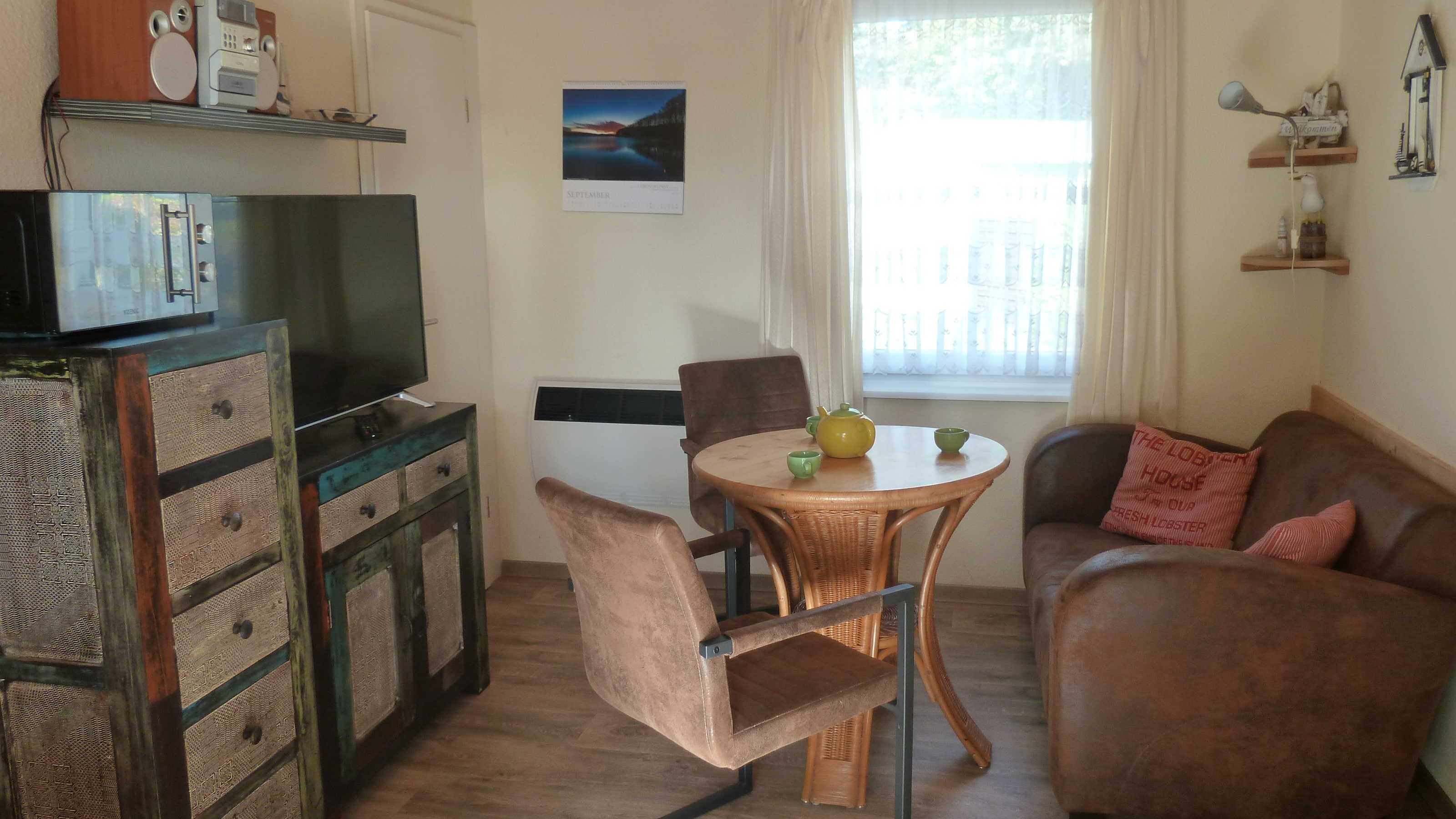 A cozy living room with a television, a dining table with chairs, a sofa, and a window with curtains.