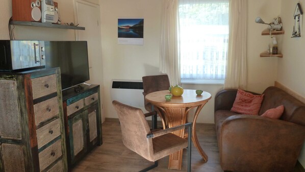 Un salon confortable avec un téléviseur, une table à manger avec des chaises, un canapé et une fenêtre avec des rideaux.