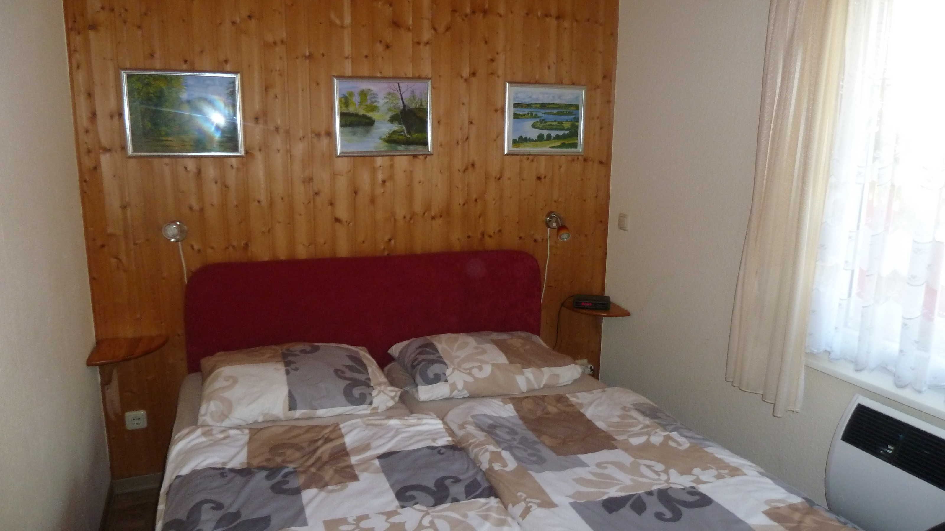 Ein Schlafzimmer mit einem Holzpaneel-Kopfteil, einem roten Kopfteil, einem Bett mit einem gemusterten Überwurf und drei gerahmten Bildern an der Wand.