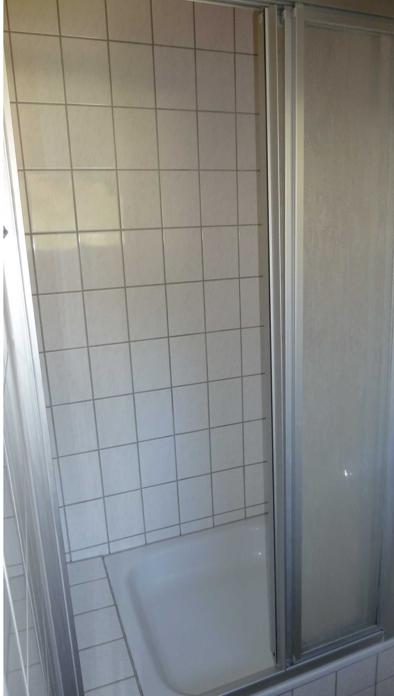 Een badkamer met witte tegels, een glazen douchecabine en een witte badkuip.