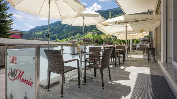 An outdoor cafe with wicker chairs and large umbrellas, overlooking a mountainous landscape.