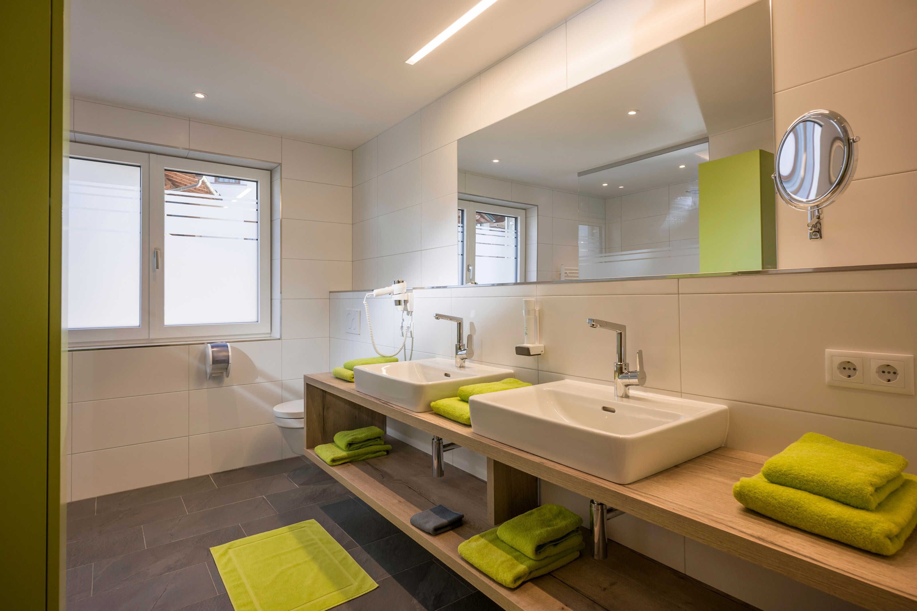 A modern bathroom with two sinks, a mirror, and a window.