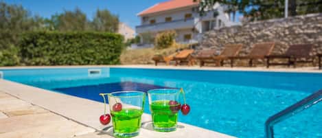 A swimming pool with two glasses of green liquid and cherries on the edge.