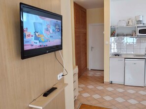 A TV mounted on a wall, a kitchen with white appliances, and a tiled floor.