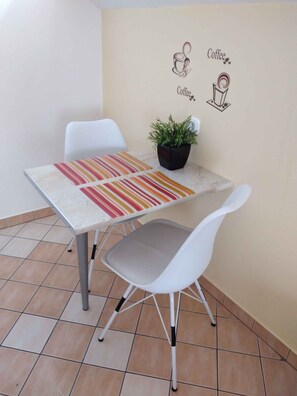 A small dining area with a table, two chairs, a striped table runner, a potted plant, and wall art depicting coffee.