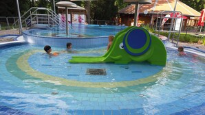 Een zwembad met een groene waterglijbaan en een rond hottubgedeelte.