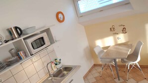 Een moderne keuken met een magnetron, waterkoker en spoelbak. Er is een zithoek met een tafel en stoelen.