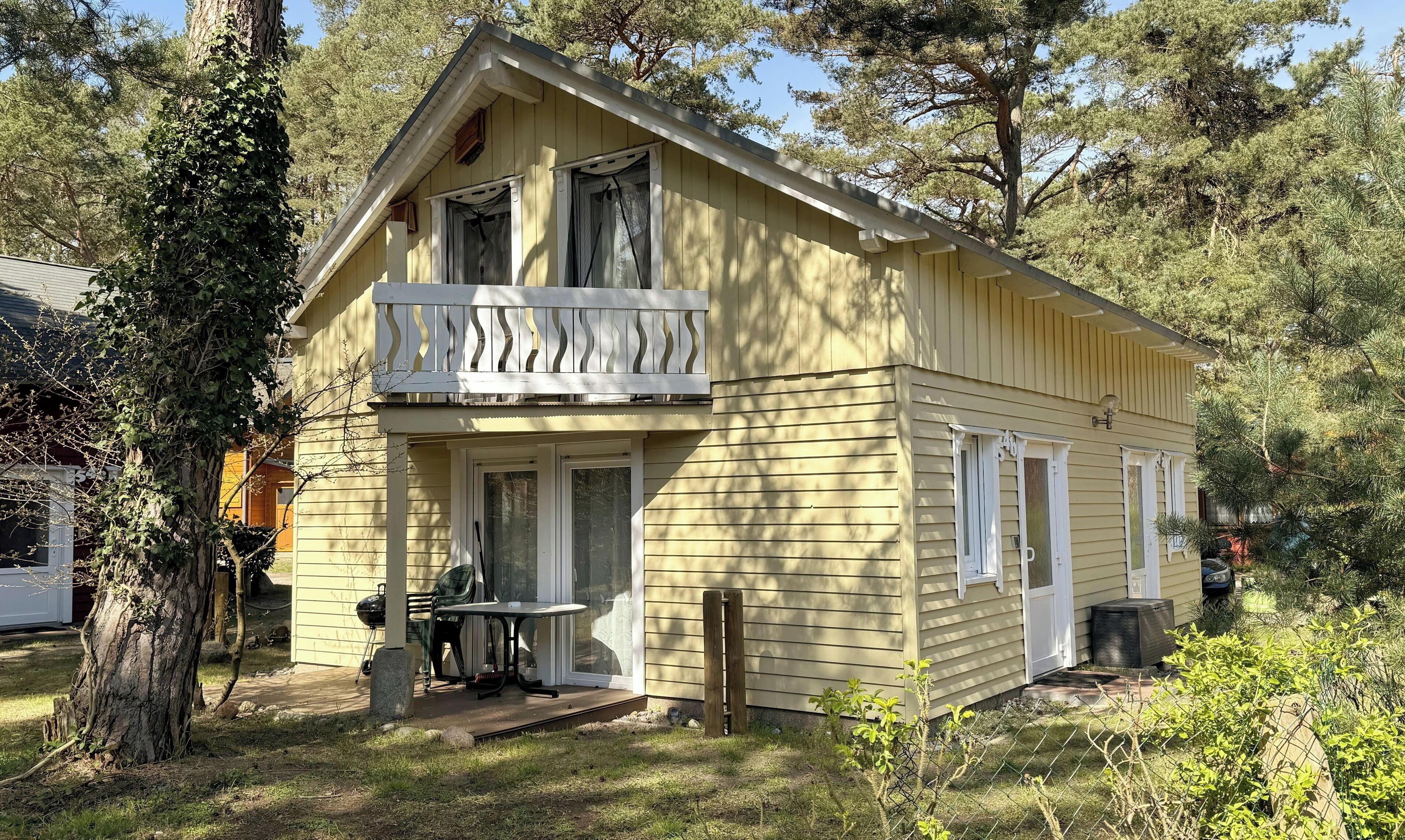 Kaksikerroksinen talo, jossa on parveke, kuisti ja pieni ulkopöytä.