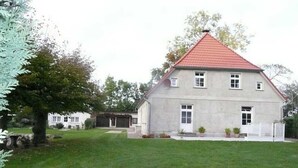 A two-story house with a red-tiled roof, a front lawn, and a white fence. - Fehaus - Ruegen-Fewo 103 (Wiek)