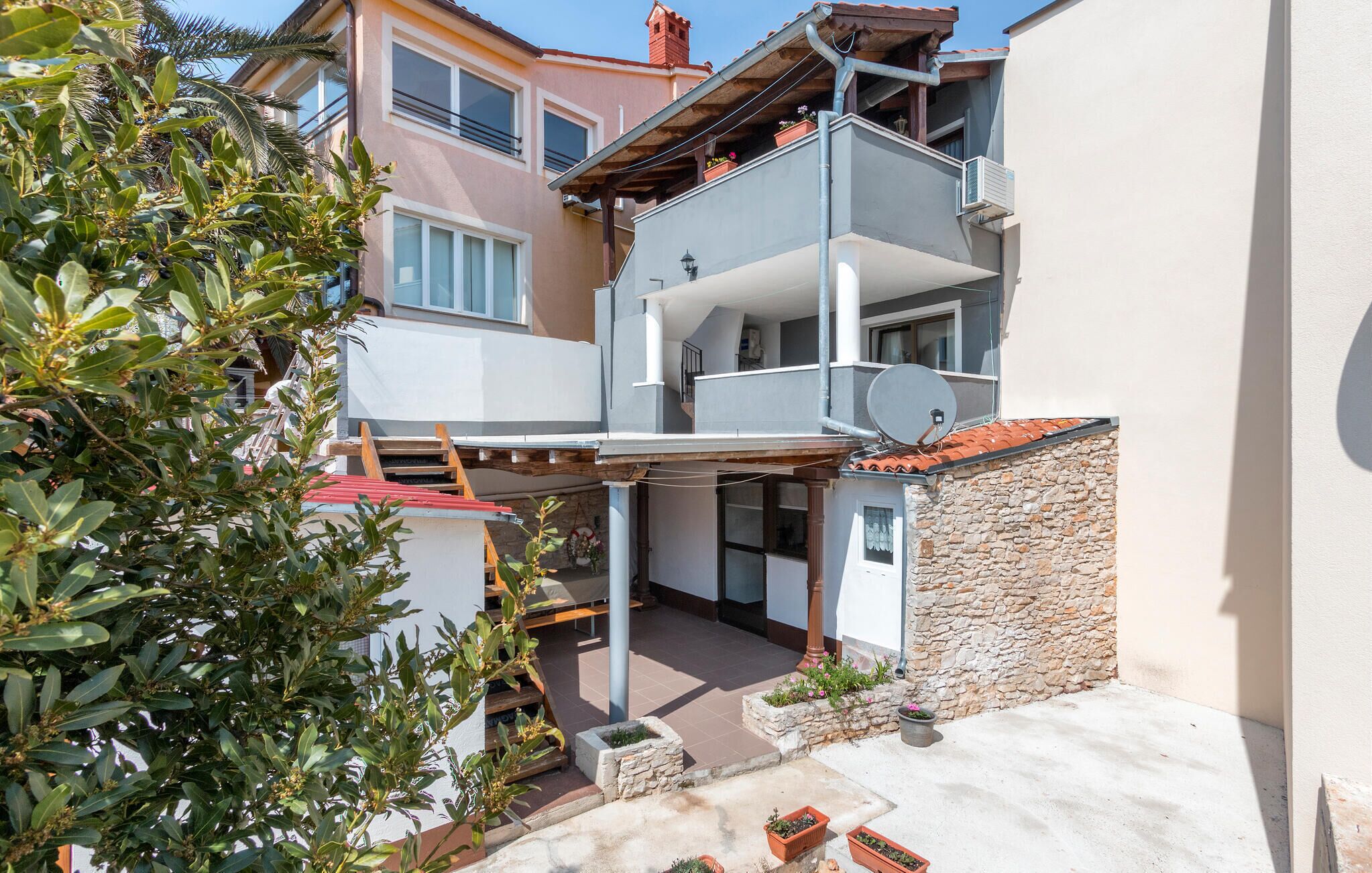 A multi-story residential building with balconies, a satellite dish, and a stone wall.