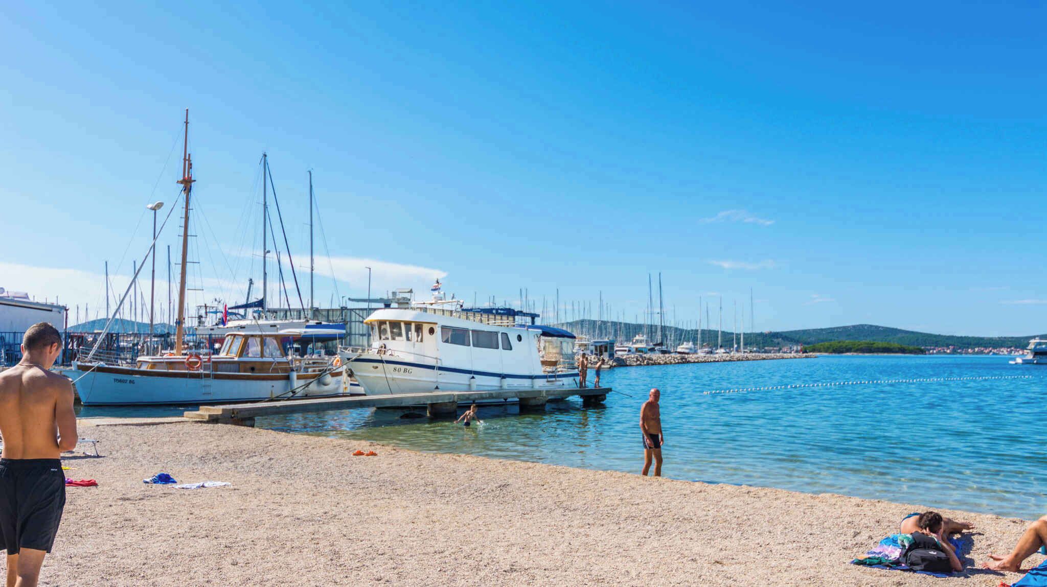 A marina with boats docked, a sandy beach, and a clear blue sky.