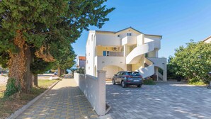 A modern two-story building with a spiral staircase, a car parked in front, and a paved driveway. - Holiday apartment with air conditioning (Biograd na Moru)