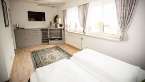 Un dormitorio con cama, cómoda, radiador, ventana con cortinas y televisor en la pared.