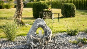 Un jardín con una escultura de piedra, un banco y setos bien cuidados.