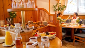 Ein Frühstücksbuffet mit verschiedenen Speisen und Getränken, Holzmöbeln und einem Fenster mit Tageslicht.