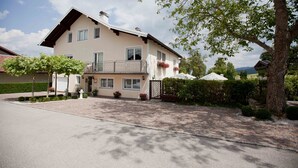 Ein zweistöckiges Haus mit Balkon, Auffahrt und einem Baum im Vordergrund.