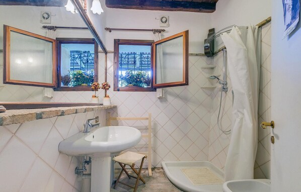 Un baño con lavamanos, espejo, ducha y un taburete pequeño.