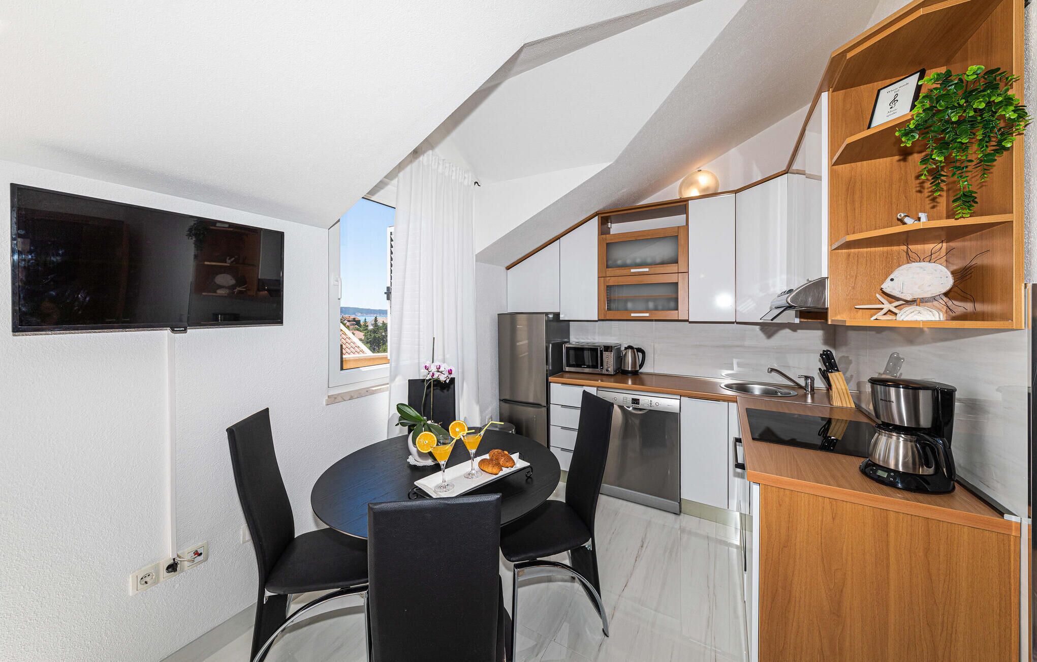 A compact kitchen with a dining area, a view through the window, and a small plant on the shelf.