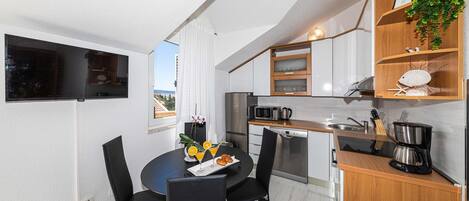 A compact kitchen with a dining area, a view through the window, and a small plant on the shelf.