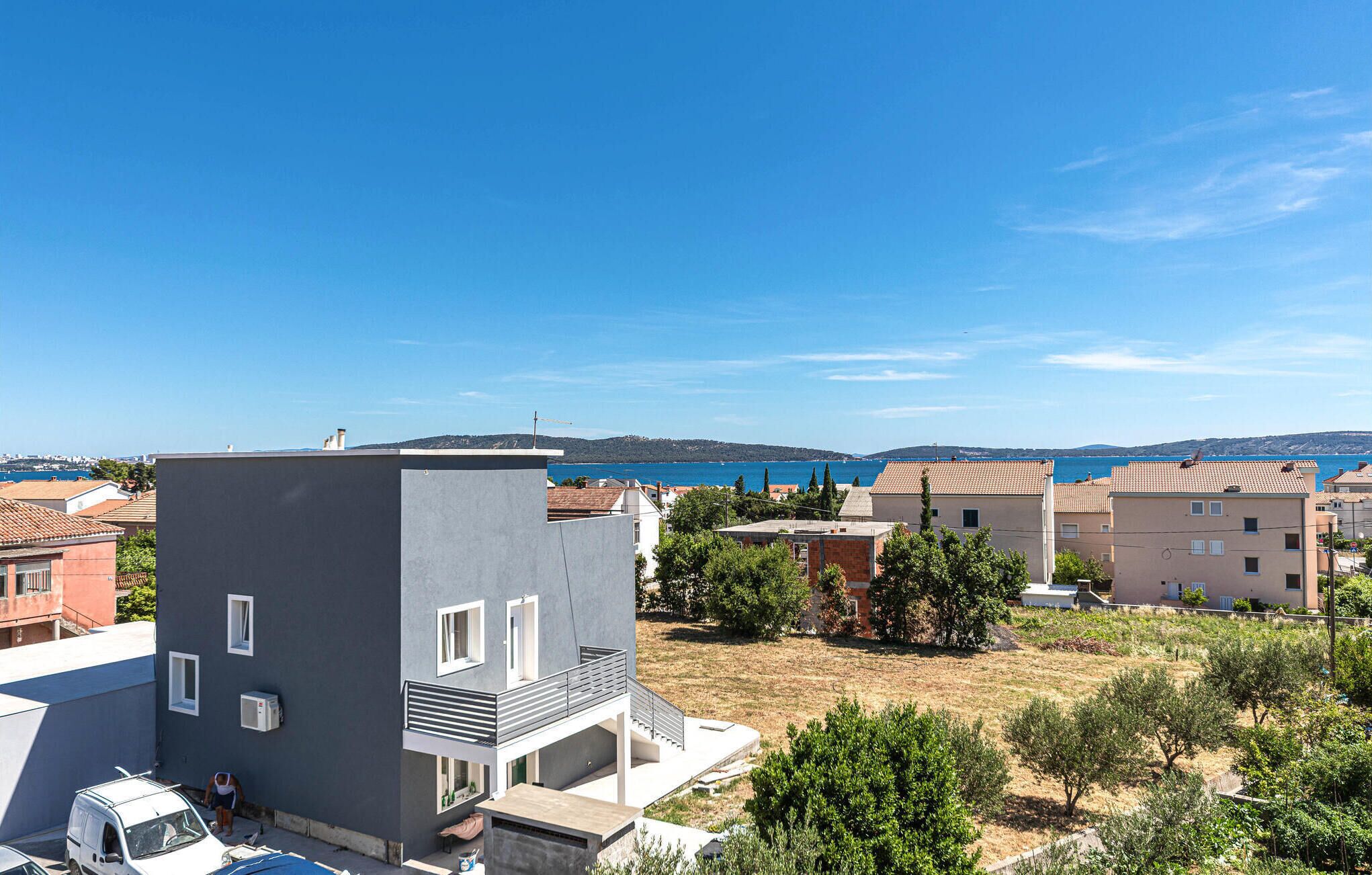 A residential area with modern buildings, a clear blue sky, and a view of the sea.