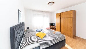 Une chambre à coucher avec un lit, une télévision, une armoire et une fenêtre avec des rideaux.