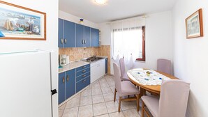 Une cuisine de taille réduite avec des meubles bleus, une table à manger avec des chaises et une fenêtre avec des rideaux.