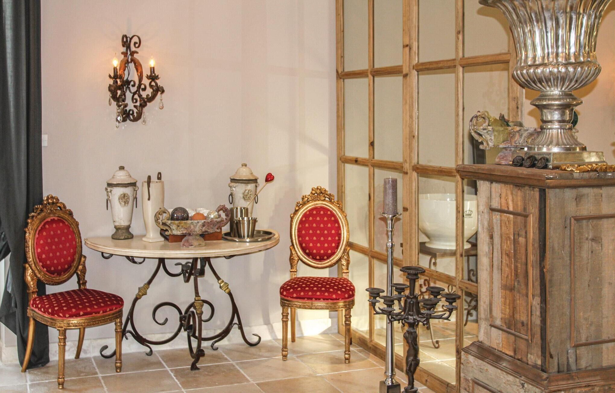 Une pièce comprenant une table ronde, deux fauteuils richement décorés, un lustre et un grand vase ornemental.