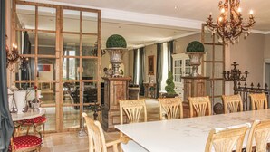 Zona pranzo con un tavolo grande e sedie decorate, un lampadario e vista su un'altra stanza attraverso una porta in vetro.