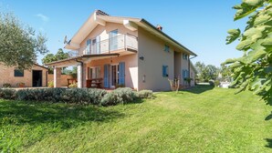 Uma casa de dois andares com varanda, alpendre coberto e gramado bem cuidado.