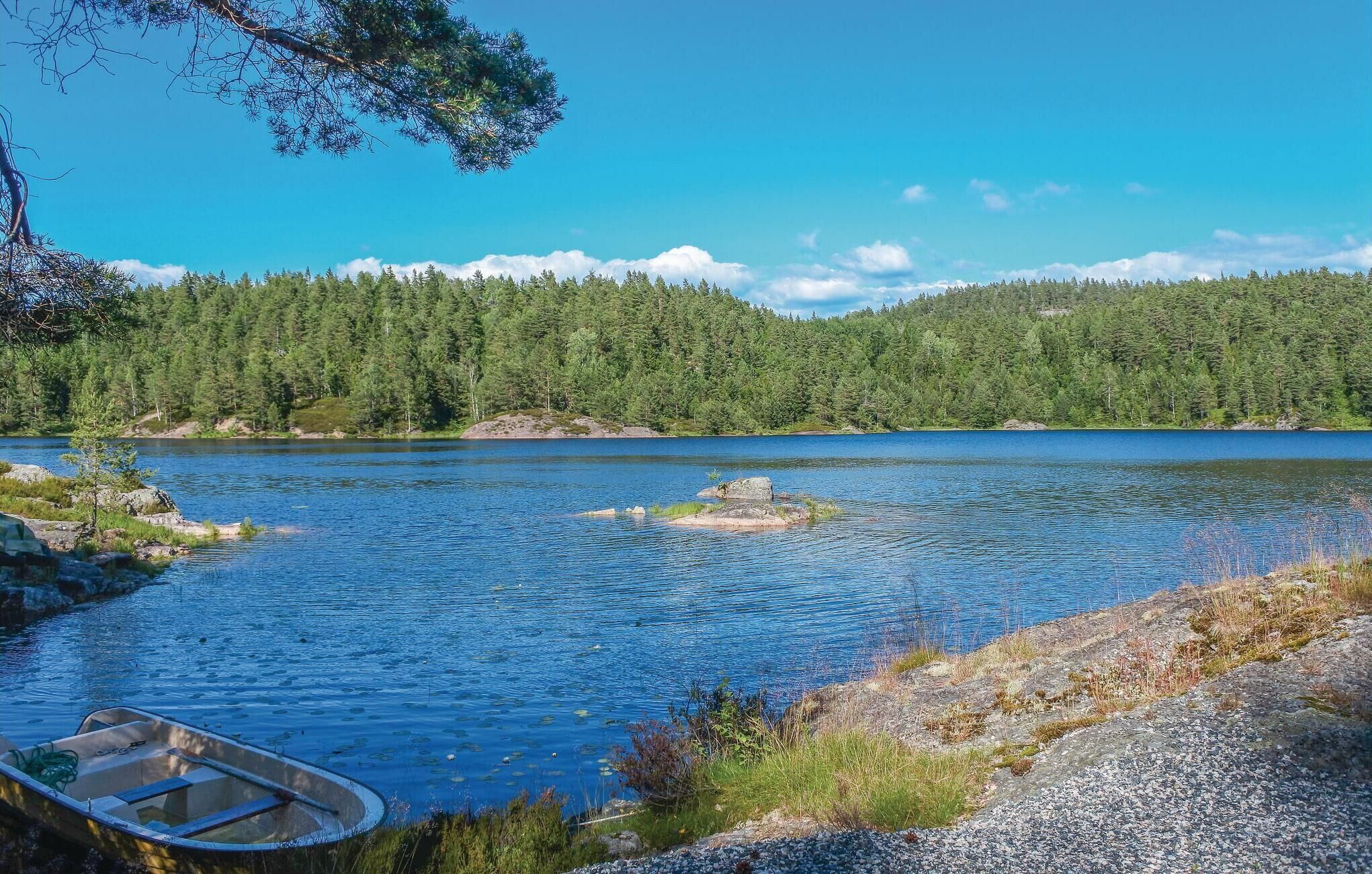 A serene lake with a small boat docked on the shore, surrounded by dense forest and rocky terrain.