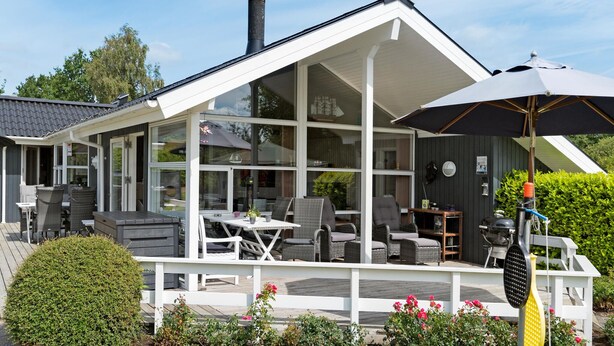 Ein modernes Haus mit einer glasverglasten Veranda, Gartenmöbeln und einem Grill.
