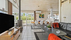 Ein modernes Wohnzimmer mit großem Flachbildfernseher, einer Essecke mit Holztisch und -stühlen, einer schwarzen Ledersofa und einer Küche im Hintergrund.