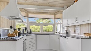 Eine moderne Küche mit weißen Schränken, einem eingebauten Backofen und einem großen Fenster mit Blick ins Grüne.