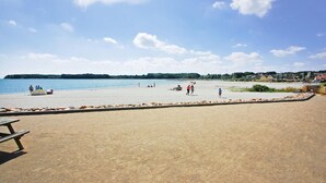 Ein Strand mit einem Sandbereich, einem Picknicktisch und einer Reihe von Felsen am Rand.