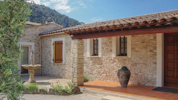 Un edificio de piedra con tejado de baldosas, una estatua en el jardín y una planta en maceta.