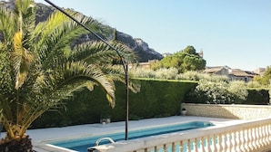 Una piscina con un muro de piedra y barandilla blanca, rodeada de vegetación y una montaña al fondo.
