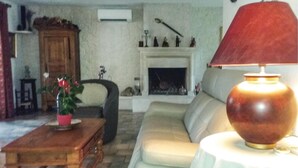 Un salón con un sofá, una mesa de centro de madera con una planta en maceta, una lámpara roja y una chimenea decorada con figuritas.