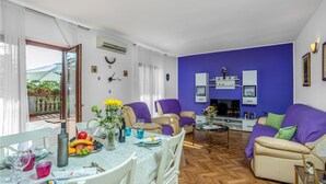 Ein Wohnzimmer mit Essbereich, mit Holzboden im Fischgrätmuster, einem großen Flachbildfernseher und einer blauen Akzentwand.