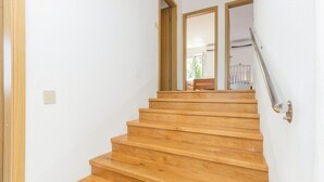 Una escalera de madera con barandilla que lleva a una habitación con una puerta blanca y un ventanal.