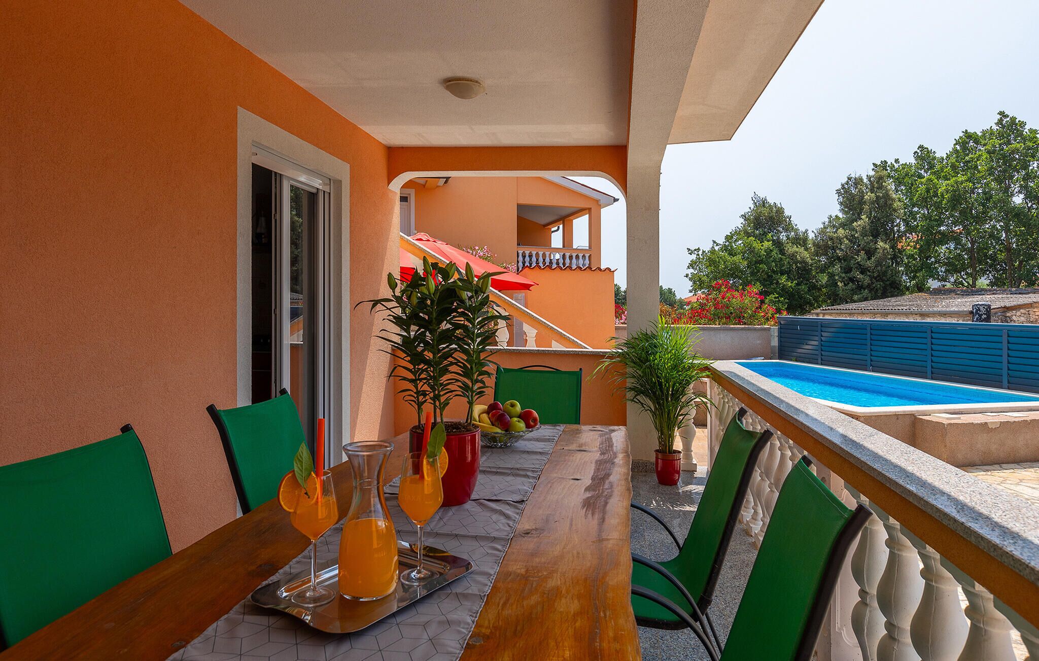 Un balcon avec une piscine, une table avec des boissons, des chaises et une plante en pot.