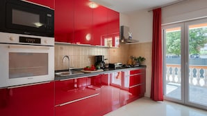 A modern kitchen with red cabinets, a microwave, a stove, and a sink. - Lovely home in Betiga (Betiga)