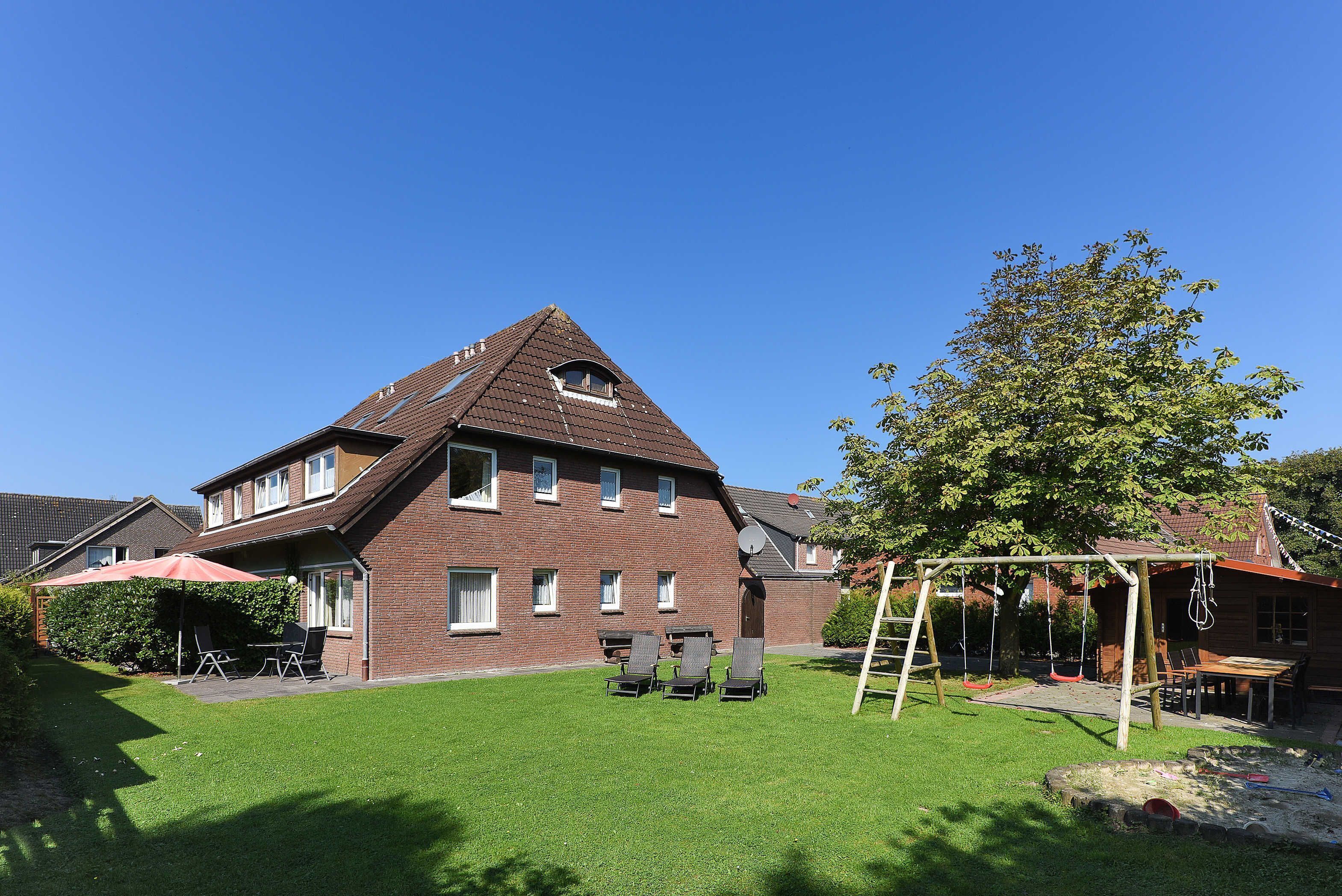 Ein Wohnhaus mit geneigtem Dach, einer Terrasse mit Gartenmöbeln und einem gepflegten Rasen.