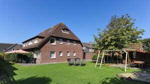 A residential building with a sloped roof, a patio with outdoor furniture, and a well-maintained lawn.