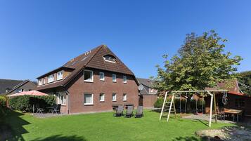Ein Wohnhaus mit geneigtem Dach, einer Terrasse mit Gartenmöbeln und einem gepflegten Rasen.