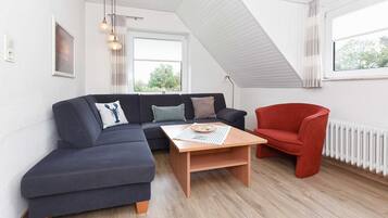 Ein modernes Wohnzimmer mit einem dunkelblauen Ecksofa, einem roten Sessel und einem Holztisch.