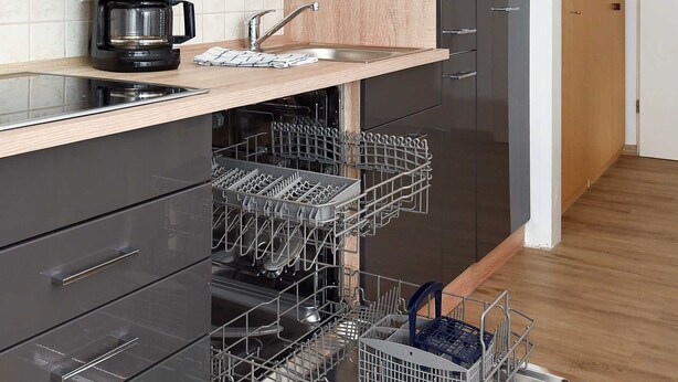 A modern kitchen with black cabinets, a wooden countertop, and a dishwasher with multiple racks.