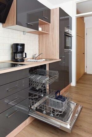 Een moderne keuken met zwarte kastjes, een houten aanrechtblad en een vaatwasser met meerdere rekken.