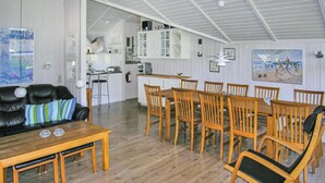 Un'ampia zona giorno con un tavolo e sedie in legno, un divano in pelle nera e una cucina sullo sfondo.