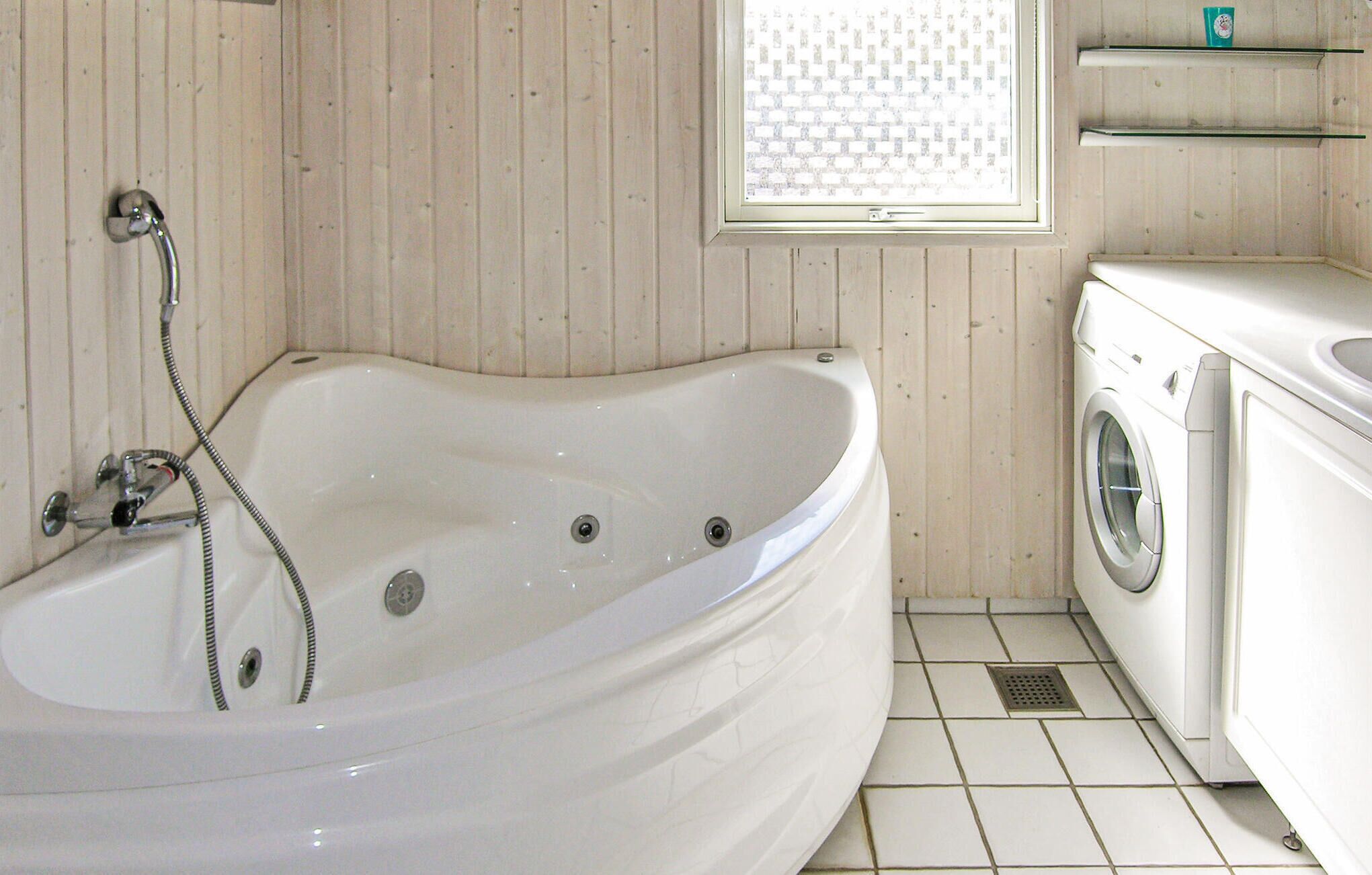 Ein Badezimmer mit einer Badewanne, einer Waschmaschine und einem Fenster mit Jalousien.
